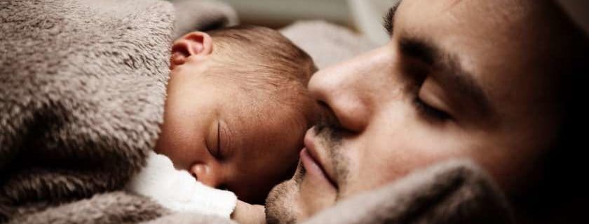 A father sleeping with his baby son sleeping on top of his chest