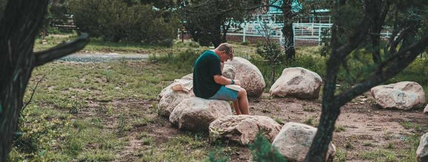 man sitting on rock reading nd quiet time with god