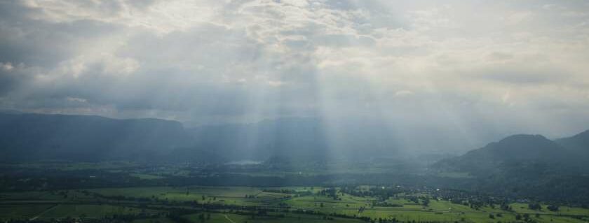 cloudy sky with rays of sunlight shining on a field below
