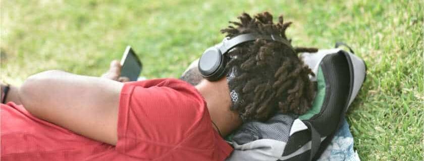 man lying on grass with headphones on and best christian audio books