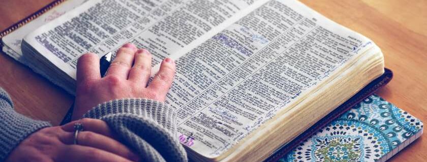 woman hands on open bible with notebook and best christian bibles