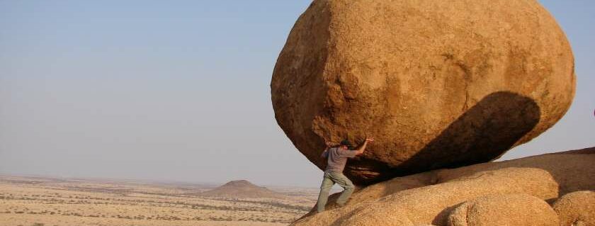 man standing beside and pushing huge rock formation
