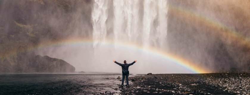 person in front of waterfalls with double rainbows and god is great god is good prayer