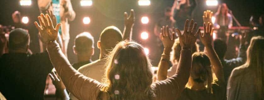 woman raising her arms in a crowd and why do we worship god