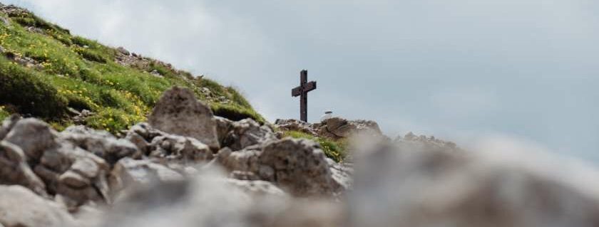 wooden cross on grey rocks under cloudy skies and crucifixion of jesus